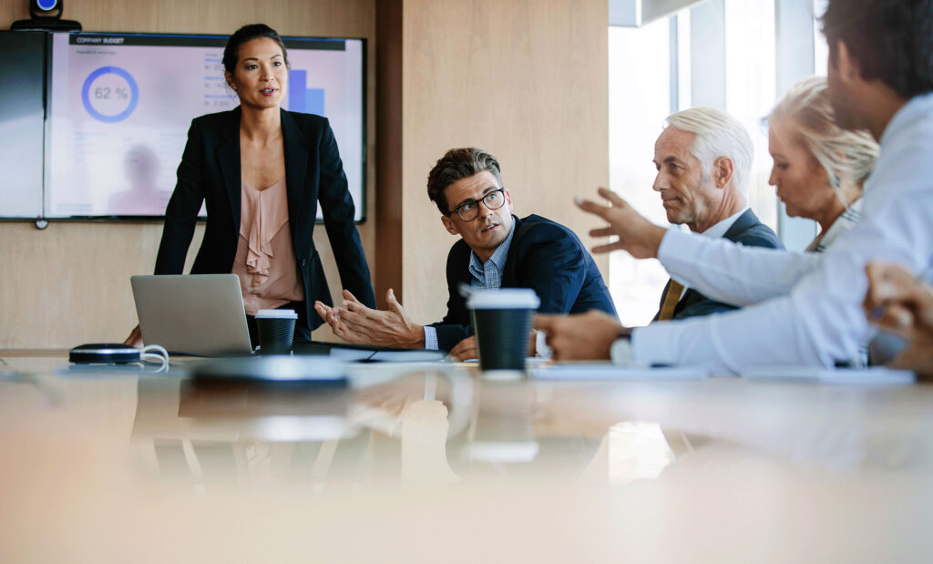 People seated around a boardroom table engaged in a discussion, highlighting the importance of collaboration and communication in a professional business meeting setting.