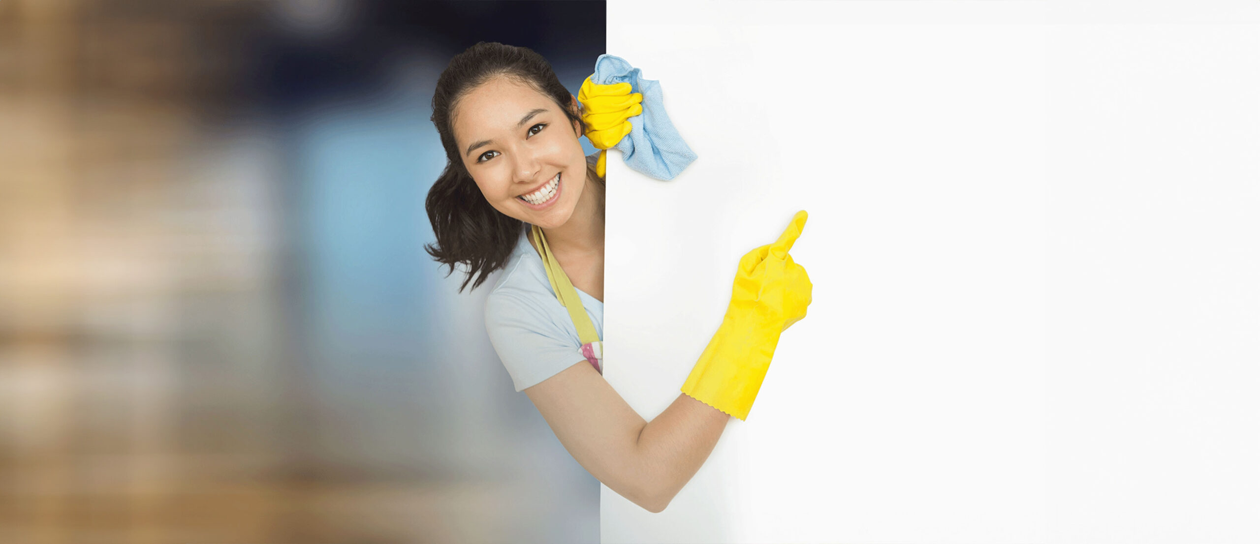 Smiling female cleaner wearing yellow gloves and holding a cleaning cloth, pointing to a blank white space, highlighting the need for domestic helper insurance coverage.
